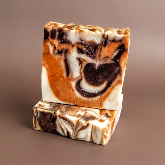 Cocoa and Turmeric soap bars with orange, cream and dark brown swirls on a warm brown background.